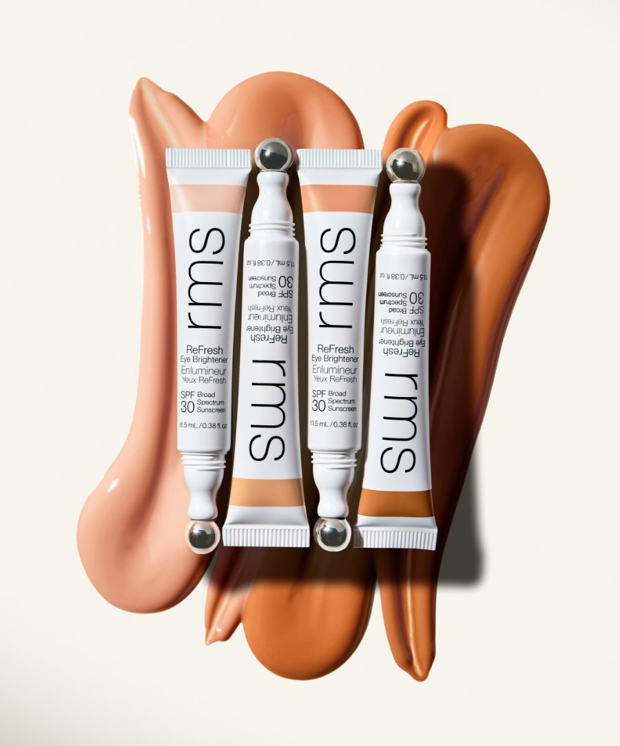 Three tubes of ReFresh Eye Brightener Broad Spectrum SPF 30 + Correcting Tint with metal applicator tips displayed on creamy swatches of different skin-toned shades, showcasing clean beauty and natural ingredients.