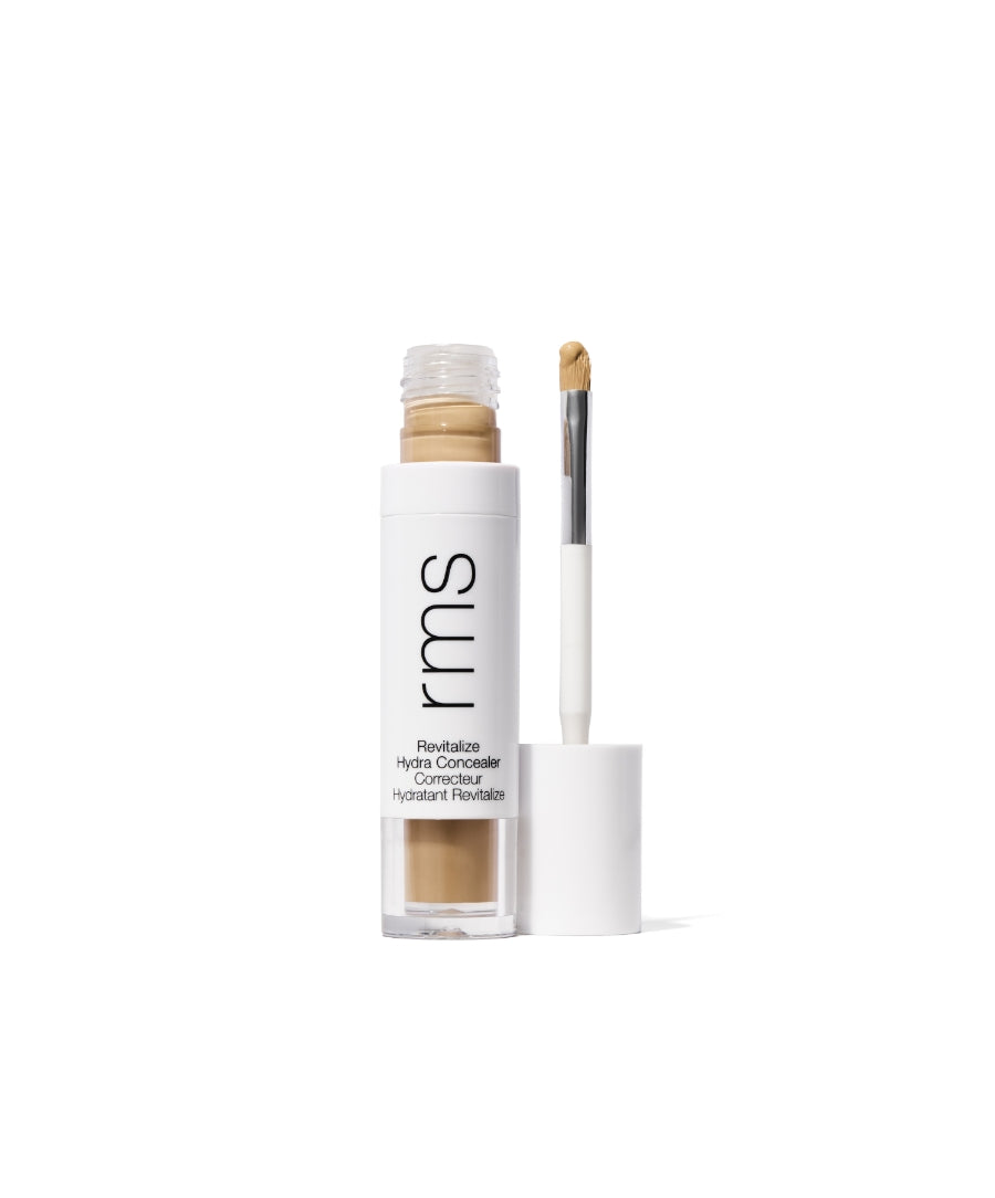 Open tube of Revitalize Hydra Concealer showing creamy light beige concealer with a white cap and built-in applicator brush, featuring minimalist packaging design.