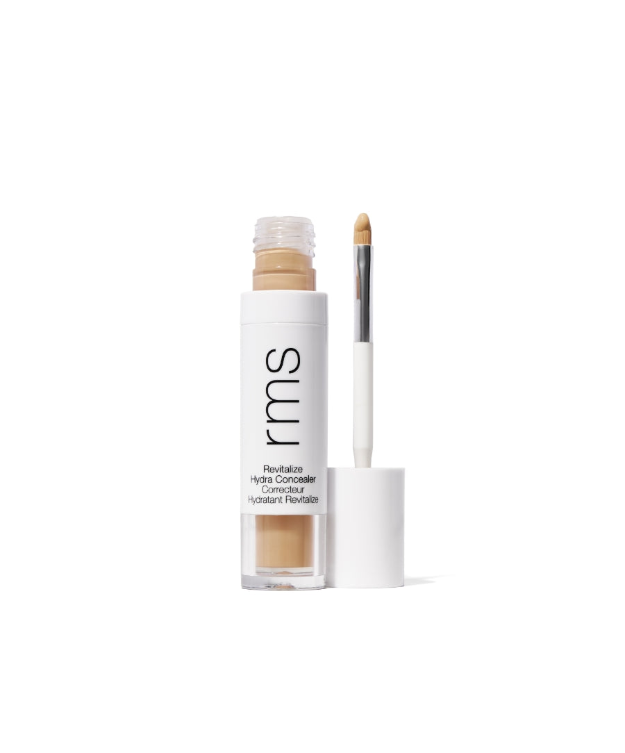 Open tube of Revitalize Hydra Concealer by RMS Beauty showing light beige creamy concealer with attached applicator brush against white background, cruelty free makeup product.