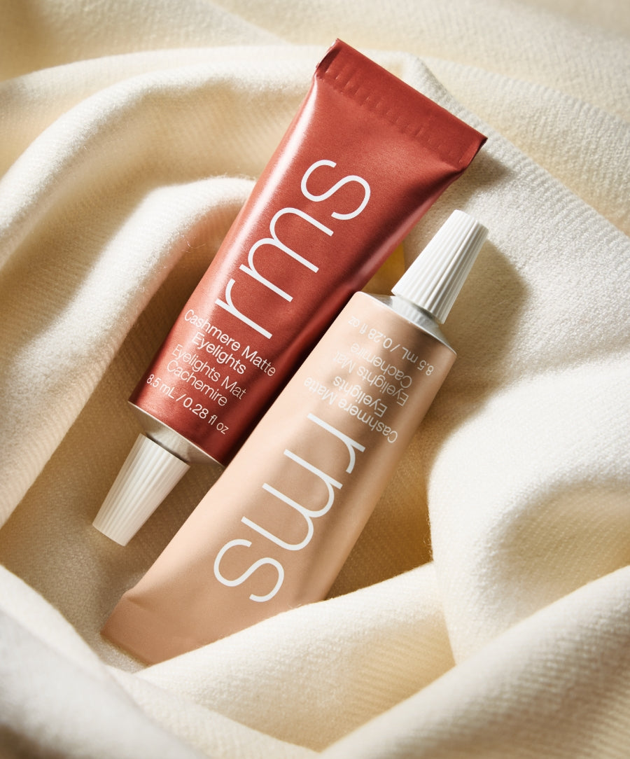Two tubes of Cashmere Matte Eyelights makeup in soft, neutral tones resting on a cozy cream-colored fabric, highlighting clean beauty and natural ingredients.