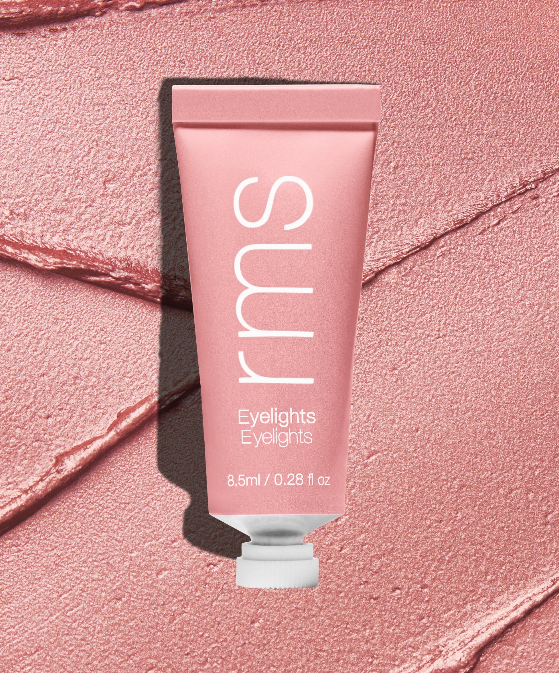 Tube of Eyelights Cream Eyeshadow in a soft, shimmery rose shade lying on a textured matching pink background, highlighting clean beauty and natural ingredients.