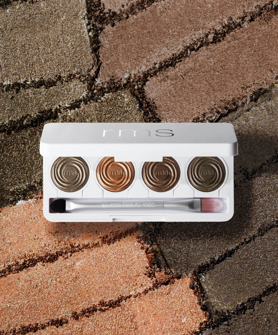 ReDimension Hydra Eyes Quartet eyeshadow palette showcasing four neutral metallic shades with a dual-ended brush, placed on a textured surface of similar colors, highlighting clean beauty and sustainable packaging.