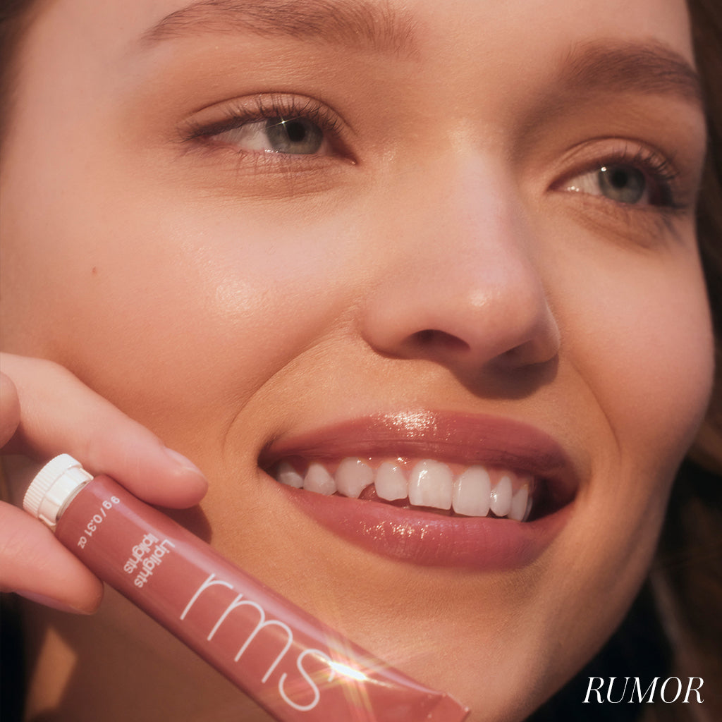 Close-up of a smiling woman holding a tube of Liplights Cream Lip Gloss in a subtle rosy shade, highlighting natural beauty with clean ingredients and cruelty free makeup.