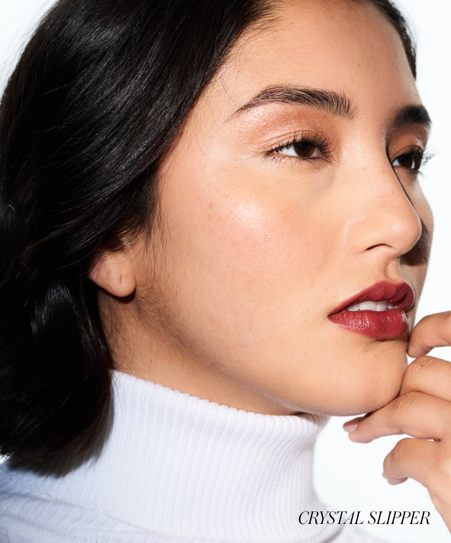 Close-up of a woman with smooth skin wearing deep red Lip2Cheek makeup, styled with natural eyebrows and a white turtleneck, showcasing clean beauty and natural ingredients.