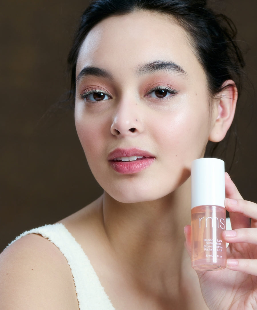 Young woman with natural makeup holding a bottle of Radiance Lock Setting Mist, showcasing its fresh and radiant finish in a clean beauty skincare setting.