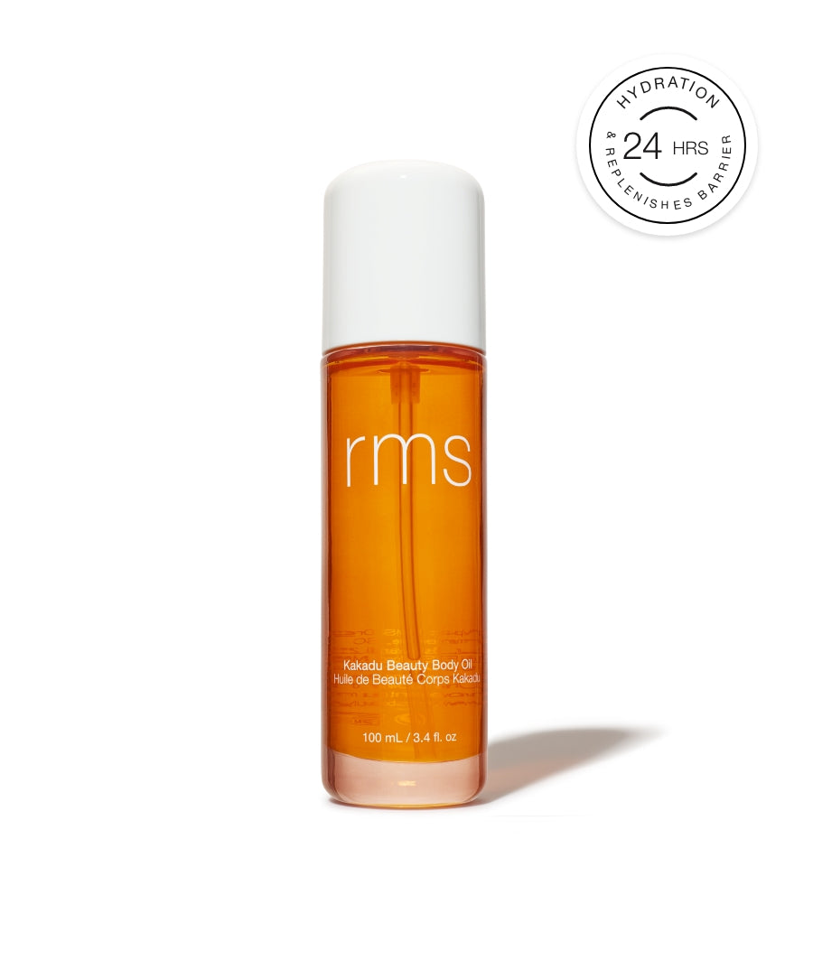 Clear glass bottle with white cap containing amber-colored Kakadu Body Oil by RMS Beauty, shown with 24-hour hydration and replenishing barrier badge.