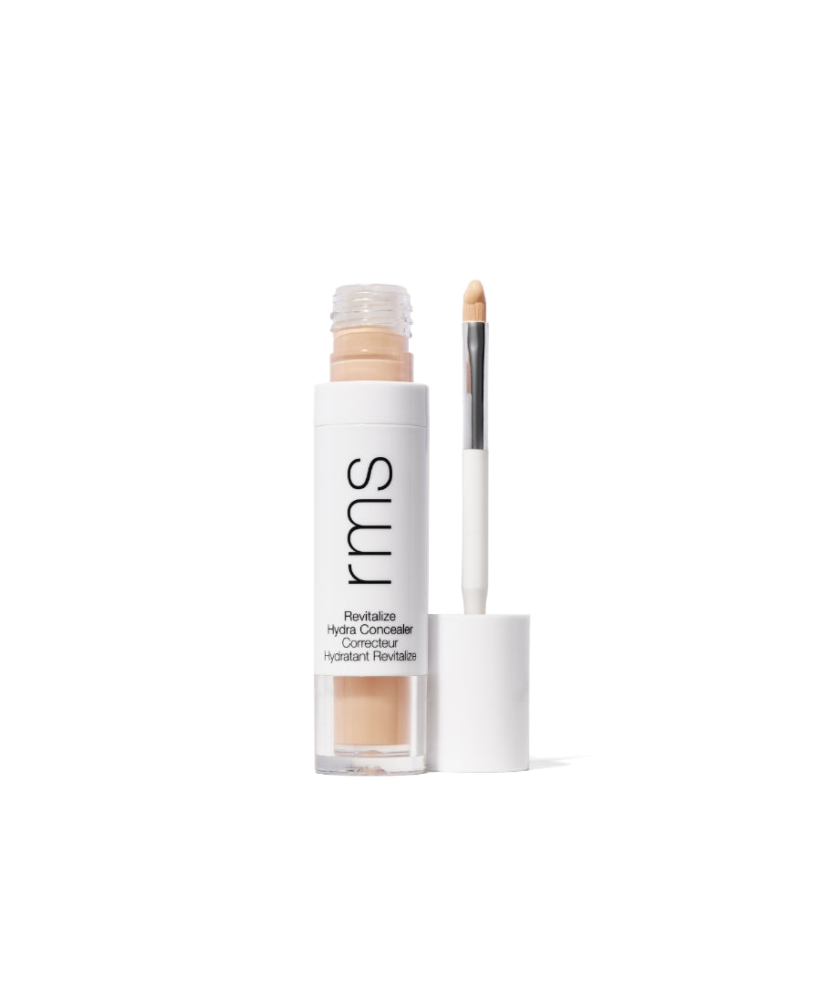 Open tube of Revitalize Hydra Concealer with doe-foot applicator showing light beige cream formula in clear and white recyclable packaging by RMS Beauty.