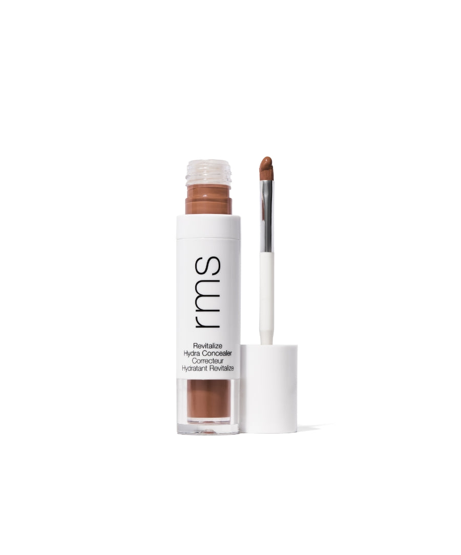 Open tube of Revitalize Hydra Concealer with visible creamy medium brown shade and attached applicator brush on white background, showcasing clean beauty makeup product.