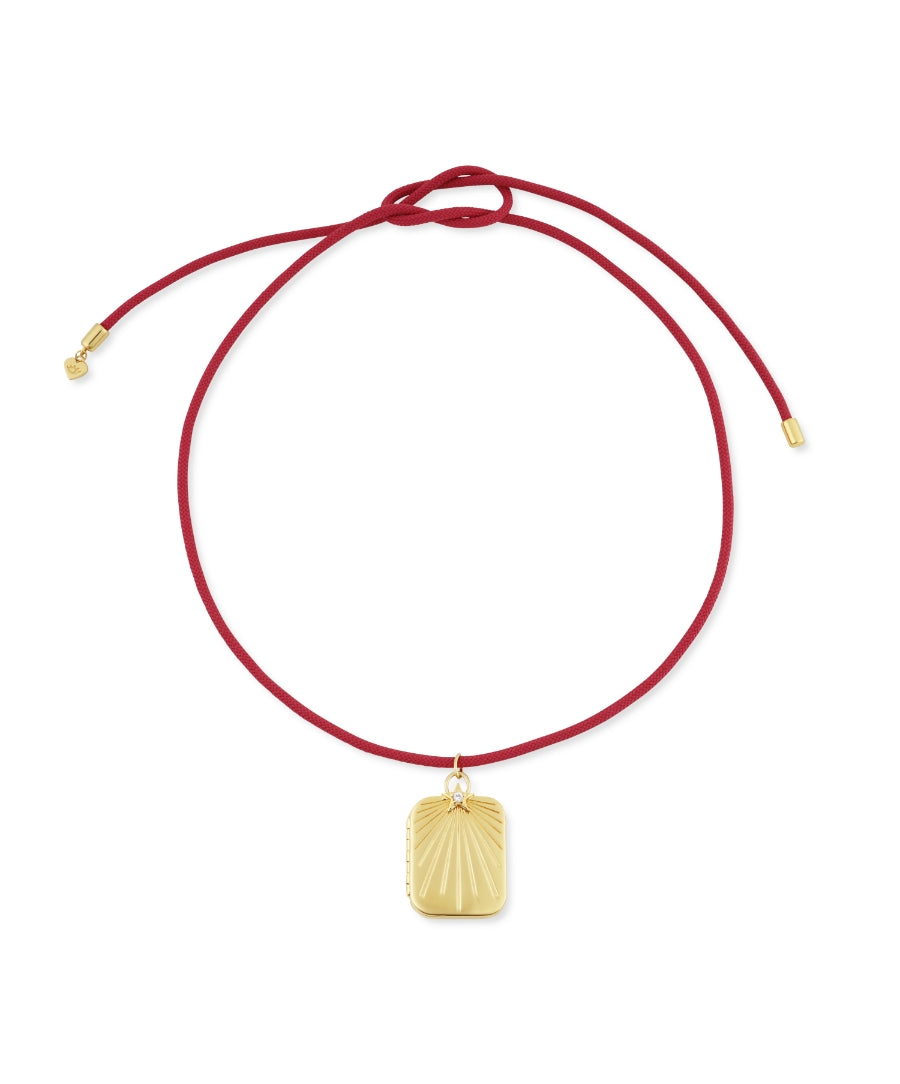 HART x RMS: Lip2Cheek Locket featuring a gold-tone engraved pendant on an adjustable deep red cord, combining elegant jewelry design with clean beauty inspiration.