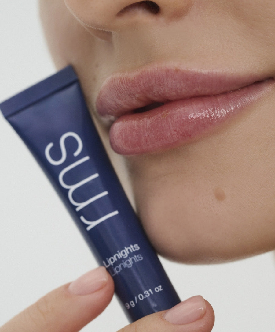 Close-up of a person holding a navy blue tube of Lipnights Overnight Lip Mask near their smooth, hydrated lips, highlighting clean beauty and natural skincare.